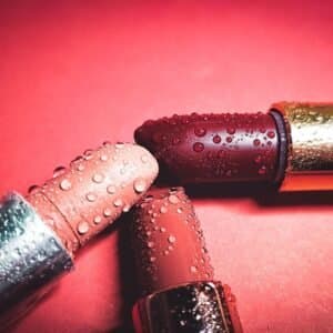 Close-up of colorful lipsticks with water droplets on a pink background, highlighting beauty.